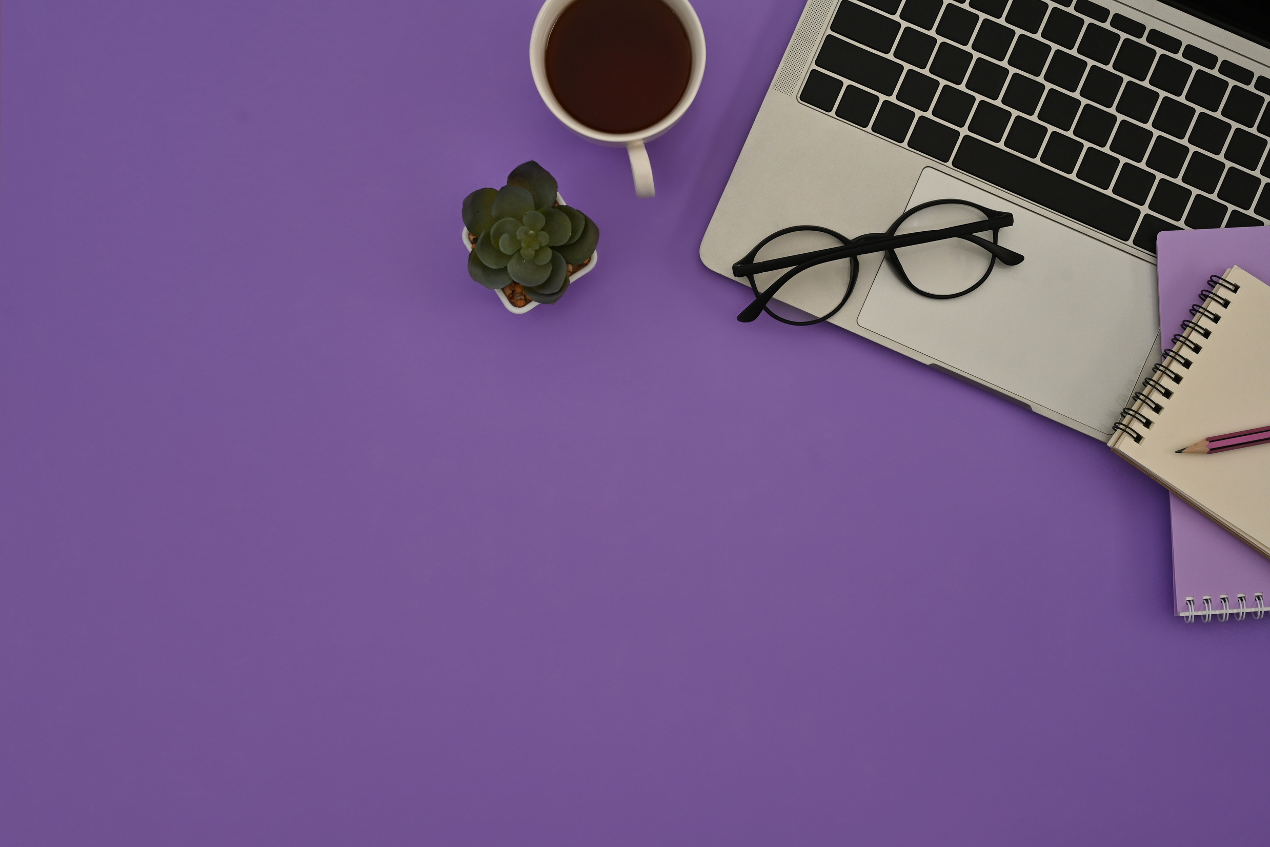 Top view of a purple desk with glasses on a laptop keyboard, a c